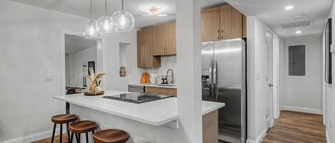 A modern kitchen with a central island, bar stools, stainless steel appliances, and pendant lighting.