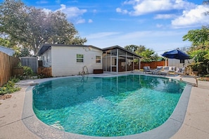 Ein Garten mit Swimmingpool, überdachter Terrasse und einem kleinen Haus.