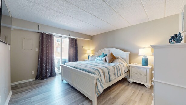 A bedroom with a bed, nightstands, a dresser, and a sliding glass door leading to a balcony. - One Bedroom, Cozy, Beachside, Retreat, with Pool! (Brigantine)