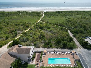 Eine Vogelperspektive eines Resorts mit Swimmingpool, Liegestühlen und einem Strandweg.