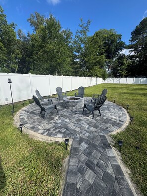 A circular outdoor seating area with Adirondack chairs and a fire pit, surrounded by a paved patio and a white fence. - Tranquil 3-bedroom house in charming Jacksonville Minutes to San Marco& Downtown (Jacksonville)