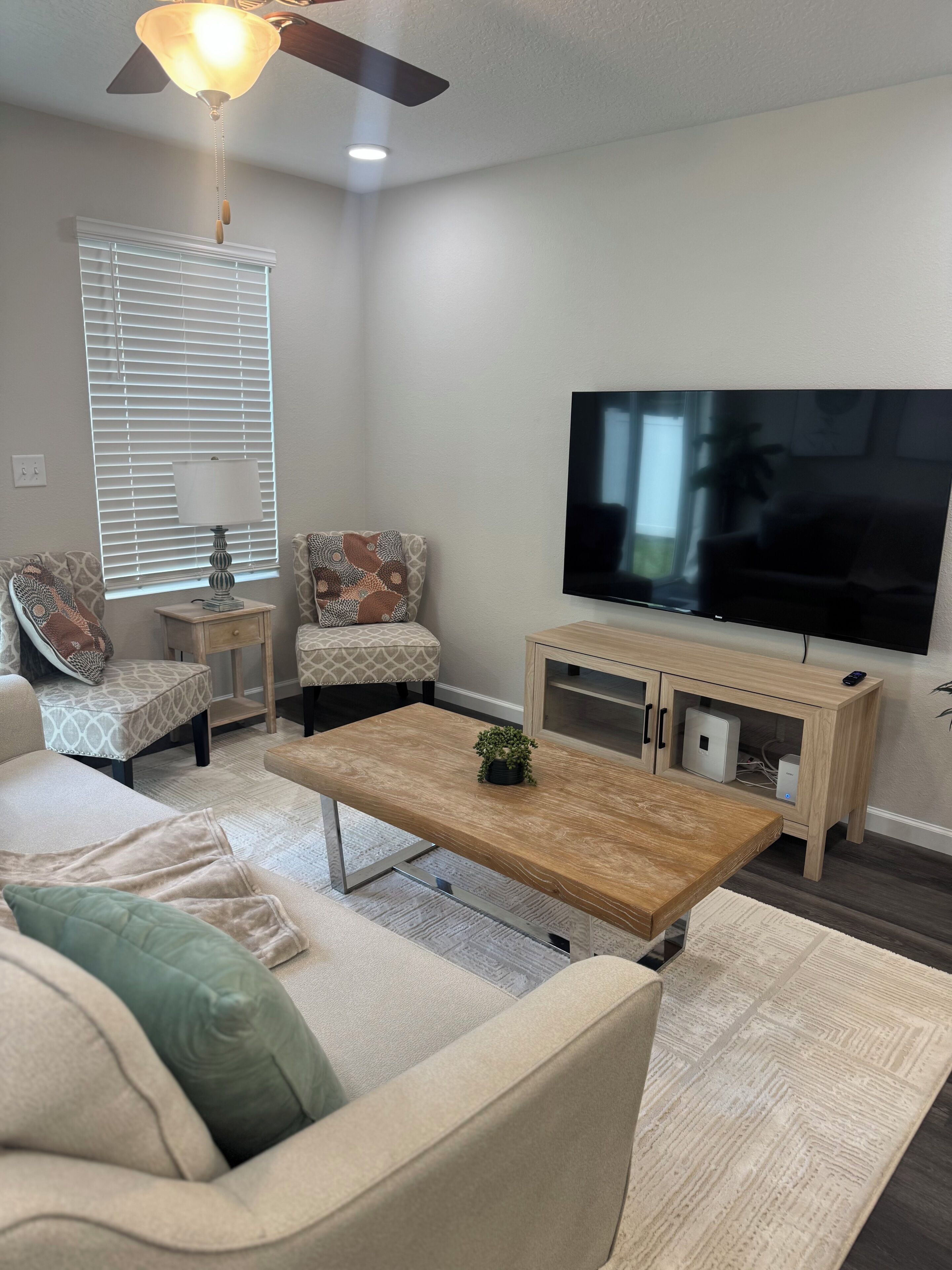 A living room with a sofa, coffee table, TV, and a ceiling fan.