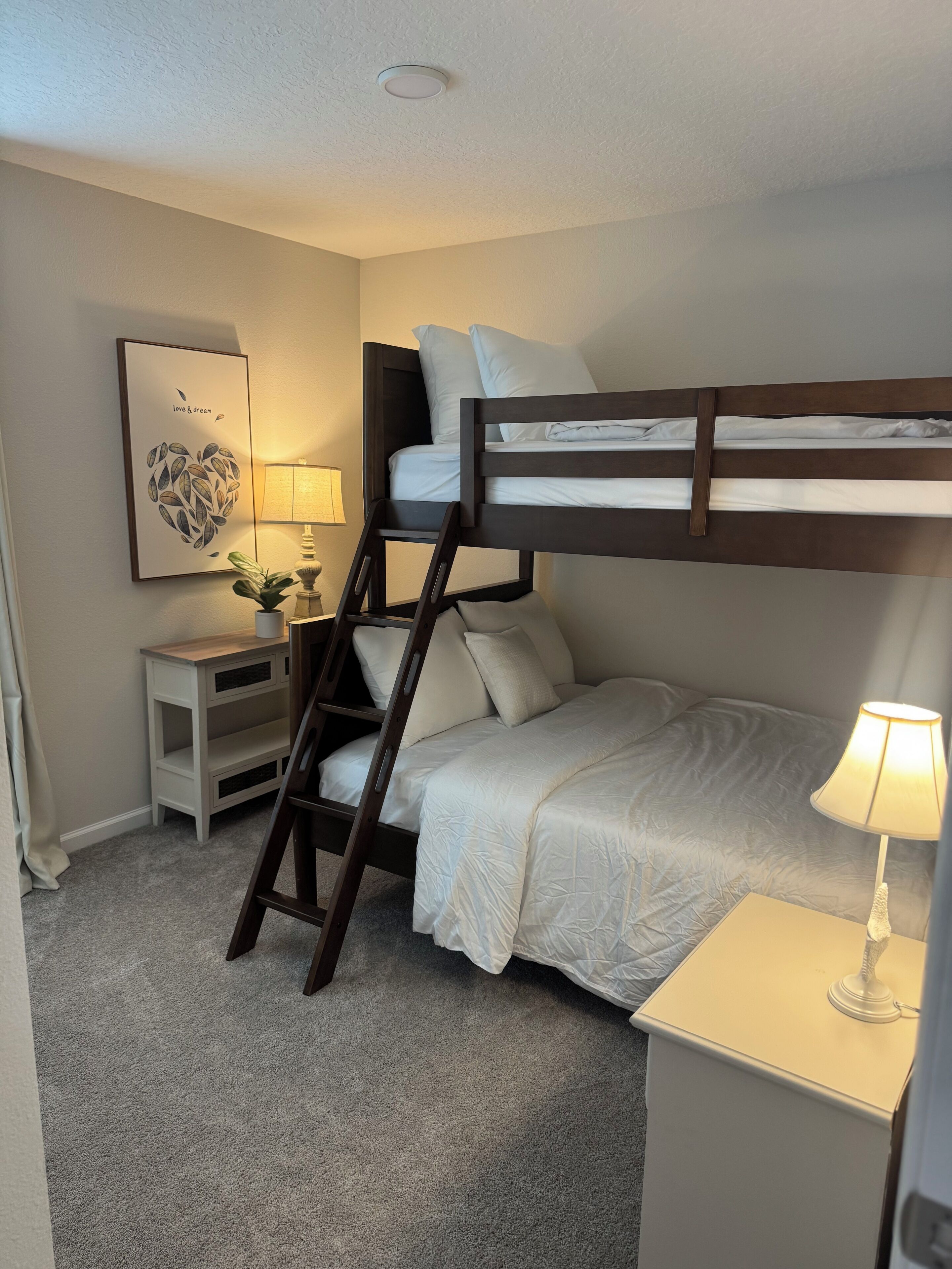 Une chambre avec un lit superposé, une échelle, une table de chevet avec une lampe, une petite étagère et un tableau accroché au mur.