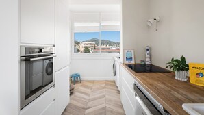 Eine kleine Küche mit Waschmaschine, einer Holz Arbeitsplatte und Blick auf eine Stadtkulisse durch ein Fenster.