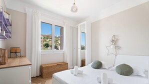 Ein Schlafzimmer mit Bett, Fenster, Nachttisch und Blick auf Gebäude.