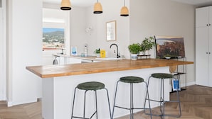 Eine moderne Küche mit einer Holztheke, Barhocker, Pendelleuchten, Blick auf die Stadt und einem Gemälde an der Wand.