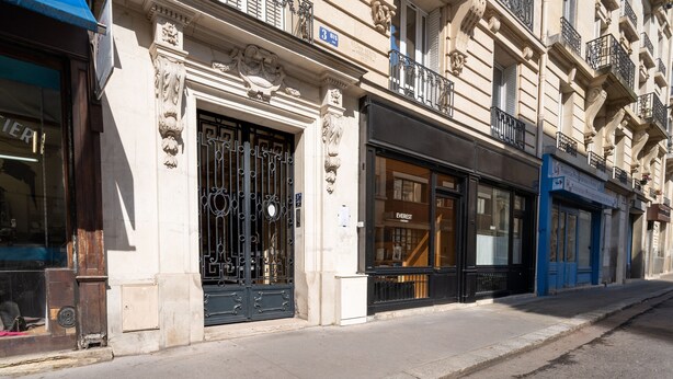Straßenansicht eines Gebäudes mit aufwendigen architektonischen Details, einem schwarzen Metallgitter und einem Schaufenster mit einem Schild.