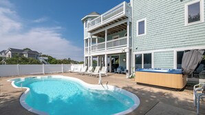En pool med buet kant, et boblebad og en toetagers bygning med balkon.