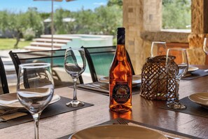 Una mesa de comedor dispuesta con copas de vino, una botella de Aperitivo Frizzantino y un jarrón decorativo.