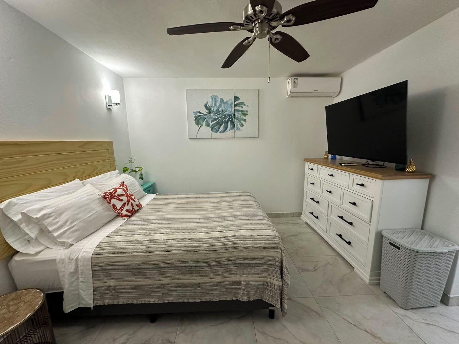 Camera da letto con un letto, una ventola a soffitto, una TV, un condizionatore d'aria a parete e un cestino.