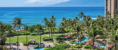 A resort with a swimming pool, palm trees, and a view of the ocean.