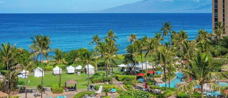 A resort with a pool, lounge chairs, palm trees, and a view of the ocean.