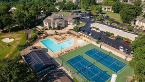 An aerial view of a residential area with a swimming pool, tennis courts, and a covered tennis facility. - Stunning 2 Bdrm/2 Bath Pointe Royale Resort & Golf (Branson)