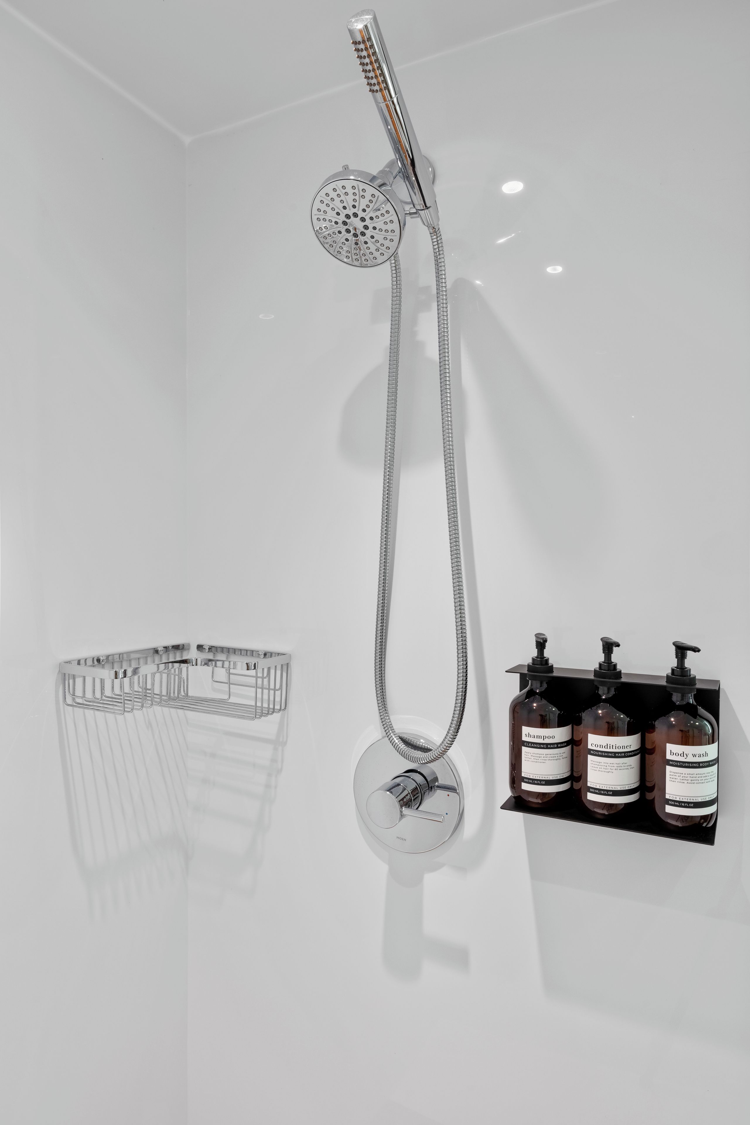 A bathroom with a shower, a hand dryer, and a soap dispenser.