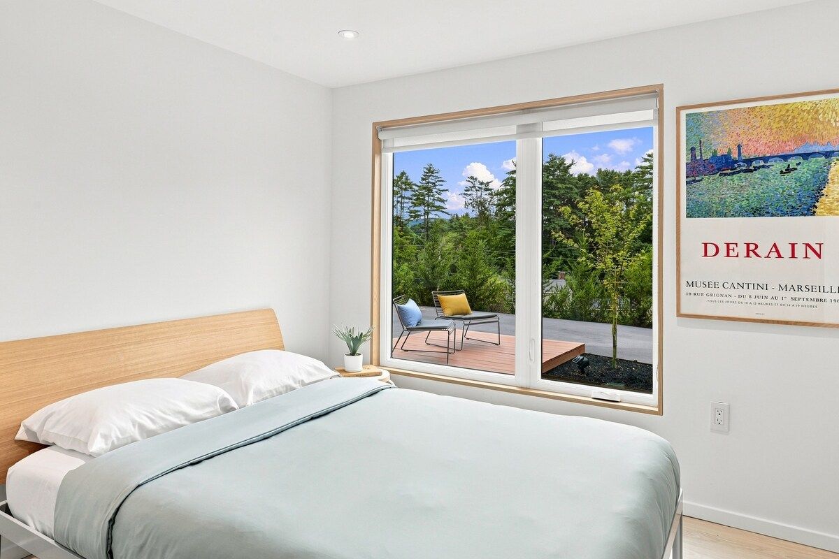 Un dormitorio con cama, ventana y vista a un espacio exterior con una silla y una mesa.