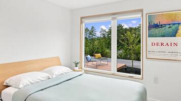 Un dormitorio con cama, ventana y vista a un espacio exterior con una silla y una mesa.