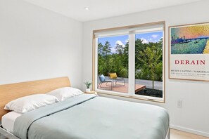 A bedroom with a bed, a window, and a view of an outdoor area with a chair and a table.