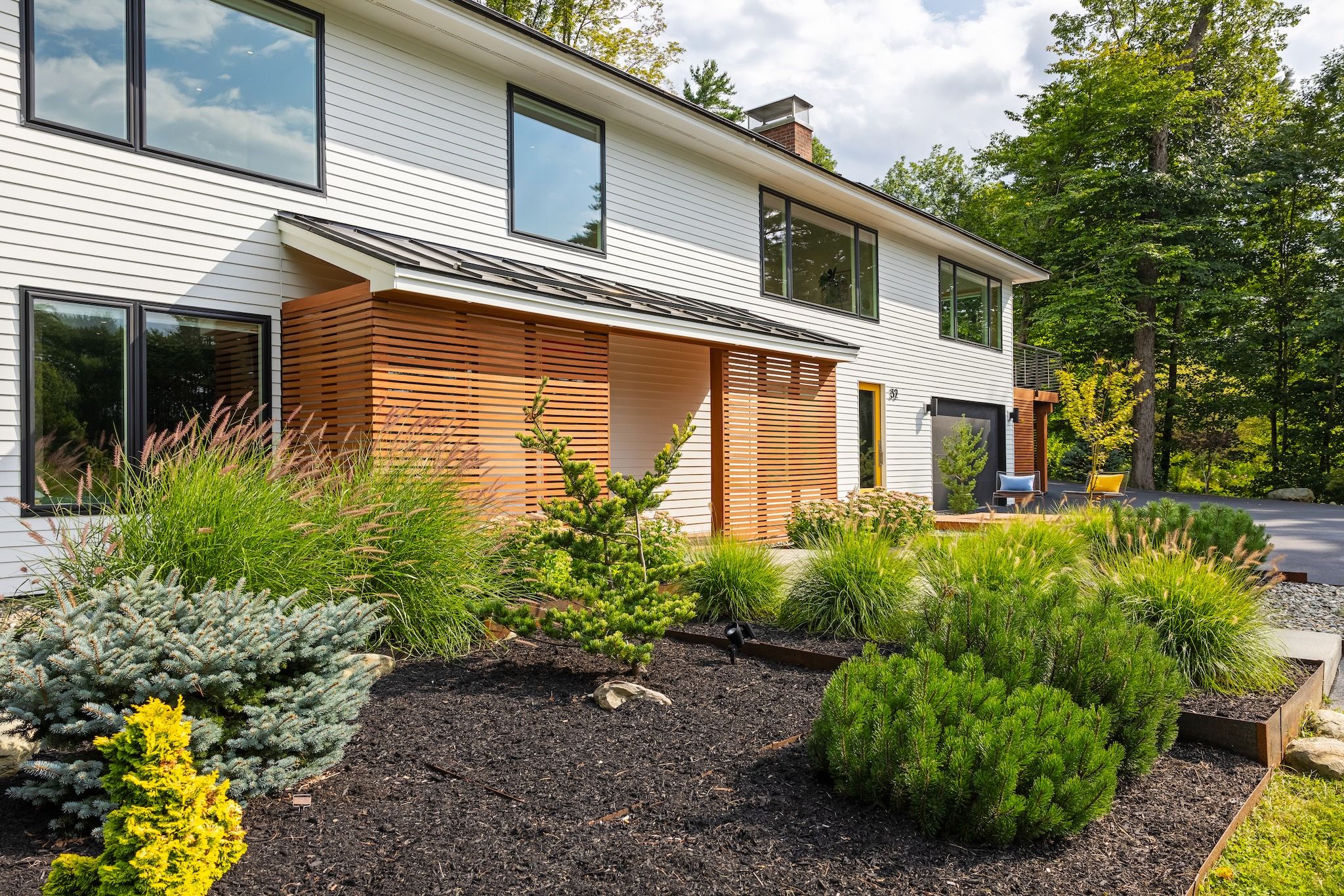 A modern two-story house with a landscaped garden featuring various shrubs and a wooden deck.