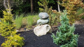 Un jardin agrémenté d’un tas de pierres, de divers arbustes et d’un petit arbre.