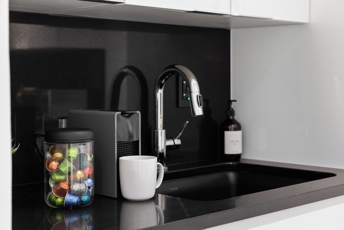 A modern kitchen with a black countertop, a stainless steel faucet, a coffee maker, and a mug.