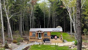 A cabin with a deck, surrounded by a forest.