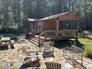 Una cabaña de madera con terraza, patio de piedra y sillas Adirondack.