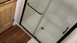 A bathroom with a wooden door, a glass shower enclosure, a white toilet, and a white sink.