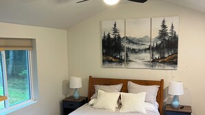 A bedroom with a bed, two nightstands, a ceiling fan, a window with blinds, and a painting of a forest.