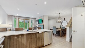 A modern kitchen with a large island, dining area with wooden furniture, and a staircase leading to another level. - Ski-In/Ski-Out Luxury with Year-Round Resort Amenities (Ludlow)