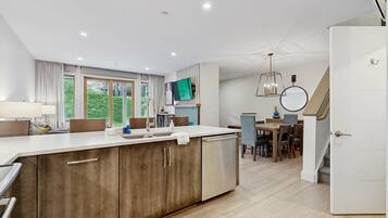 A modern kitchen with a large island, dining area with wooden furniture, and a staircase leading to another level.