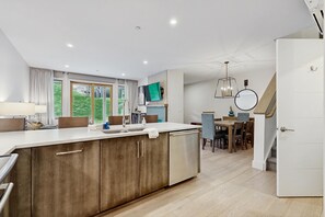 A modern kitchen with a large island, dining area with wooden furniture, and a staircase leading to another level. - Ski-In/Ski-Out Luxury with Year-Round Resort Amenities (Ludlow)