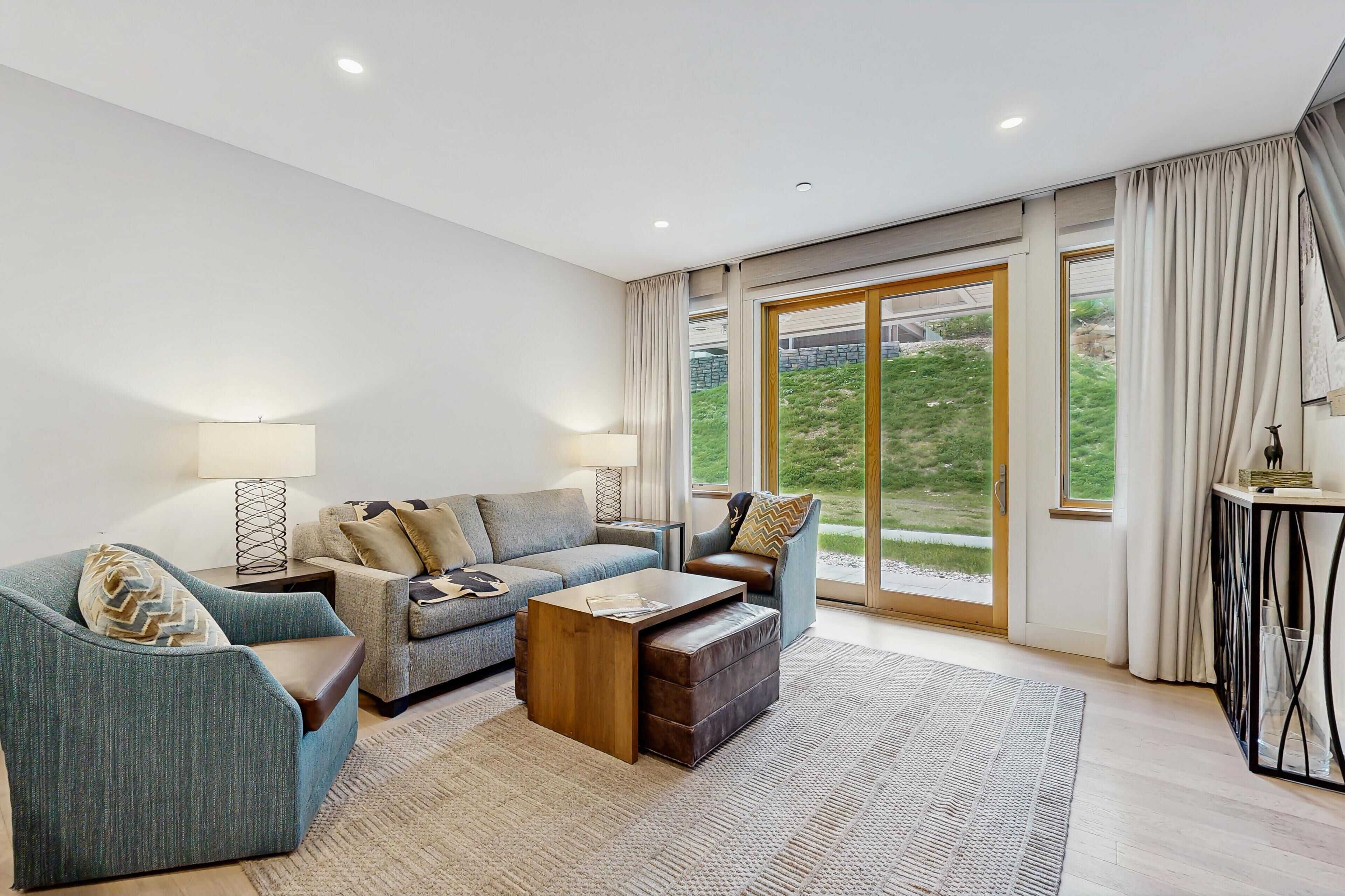 Un salon moderne avec un canapé, un fauteuil, une table basse et une vue dégagée grâce à de grandes portes-fenêtres coulissantes.