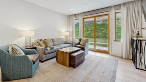A modern living room with a sofa, armchair, coffee table, and a view through large sliding glass doors. - Ski-In/Ski-Out Luxury with Year-Round Resort Amenities (Ludlow)