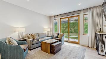 A modern living room with a sofa, armchair, coffee table, and a view through large sliding glass doors.