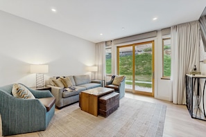 A modern living room with a sofa, armchair, coffee table, and a view through large sliding glass doors. - Ski-In/Ski-Out Luxury with Year-Round Resort Amenities (Ludlow)