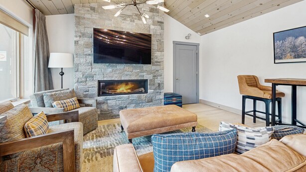 A living room with a stone fireplace, wooden ceiling, and a flat-screen TV mounted above it. - Ski-In/Ski-Out Luxury with Year-Round Resort Amenities (Ludlow)