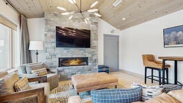 A living room with a stone fireplace, wooden ceiling, and a flat-screen TV mounted above it.