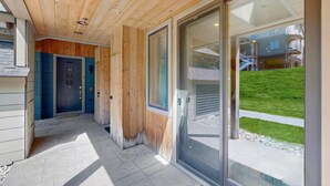 A wooden exterior with a glass door leading to a covered area with a view of a building and a grassy area. - Ski-In/Ski-Out Luxury with Year-Round Resort Amenities (Ludlow)