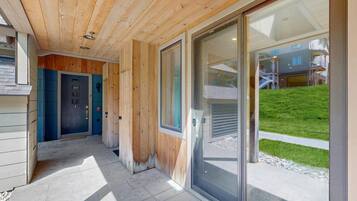 A wooden exterior with a glass door leading to a covered area with a view of a building and a grassy area.