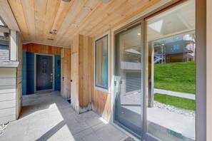 A wooden exterior with a glass door leading to a covered area with a view of a building and a grassy area. - Ski-In/Ski-Out Luxury with Year-Round Resort Amenities (Ludlow)
