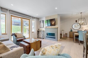A modern living room with a fireplace, a television, and a dining area. - Ski-In/Ski-Out Luxury with Year-Round Resort Amenities (Ludlow)