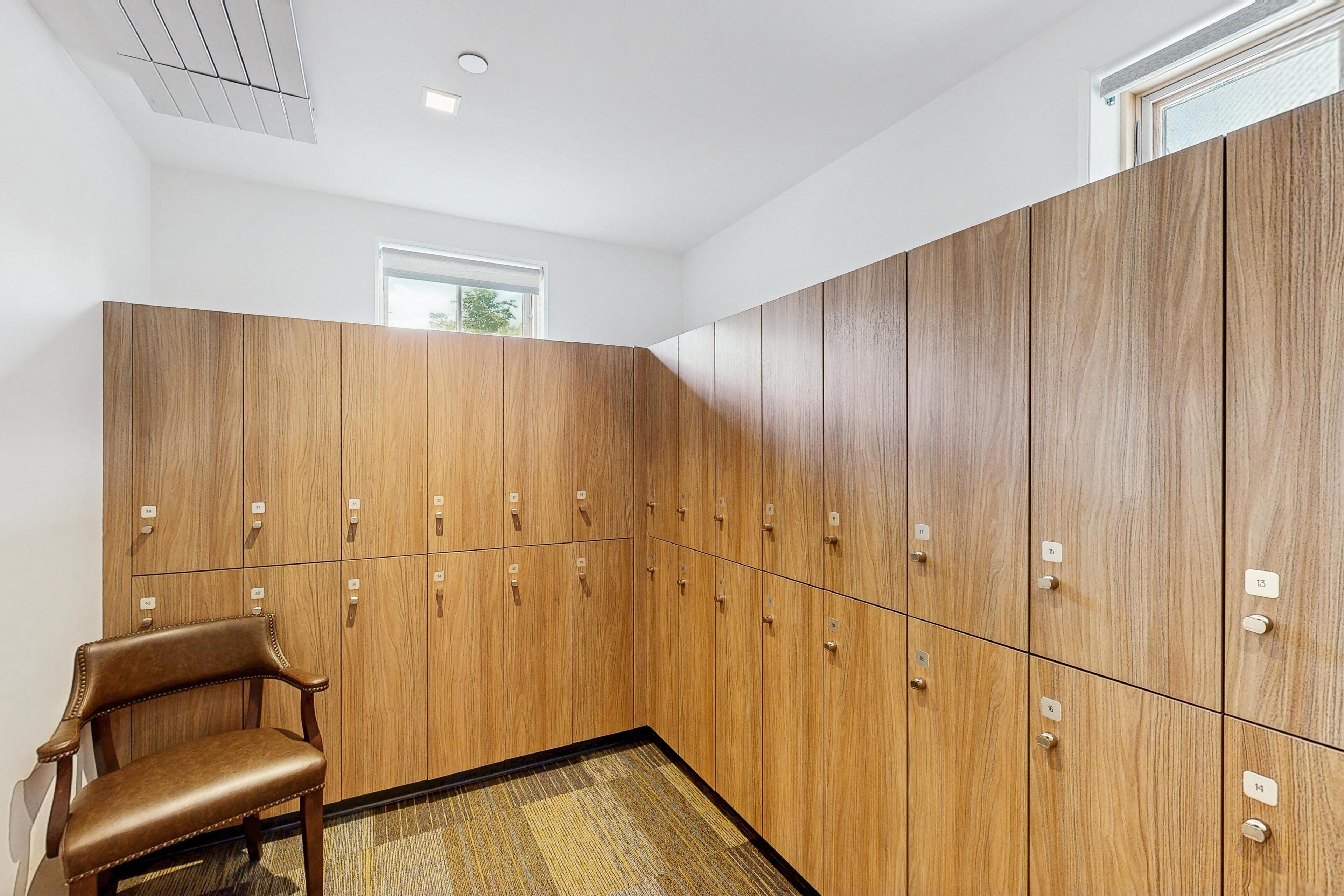 A locker room with wooden lockers, a brown leather chair, and a window providing natural light.