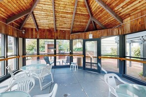 Eine überdachte Terrasse mit Glastischen und -stühlen, Holzbalken an der Decke und großen Fenstern.