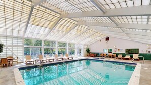 Ein Innenpool mit Glasdecke, Liegestühlen und Fliesenboden.