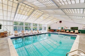 Ein Innenpool mit Glasdecke, Liegestühlen und Fliesenboden.