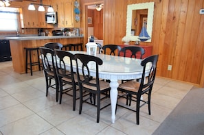 A kitchen with wooden cabinets, a central island with bar stools, a round dining table with chairs, and a red cabinet. - Ina's Place - Second Row in Garden City Beach (Garden City)