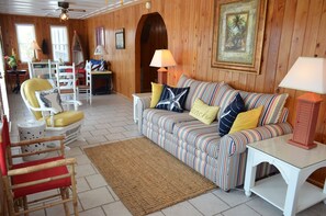A cozy living room with a striped sofa, a red chair, a white table, and a wooden door. - Ina's Place - Second Row in Garden City Beach (Garden City)