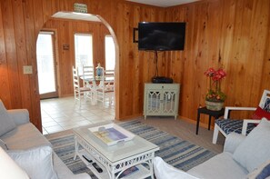A wooden-paneled room with a television, a dining table with chairs, and a sofa. - Ina's Place - Second Row in Garden City Beach (Garden City)