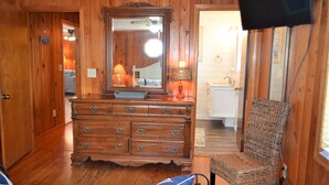 Een kamer met houten lambrisering, een dressoir, een stoel, een aan de muur bevestigde televisie en een zichtbare badkamedeur.