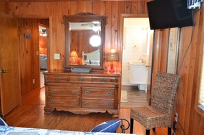 A wooden-paneled room with a dresser, a chair, a television mounted on the wall, and a visible bathroom door. - Ina's Place - Second Row in Garden City Beach (Garden City)